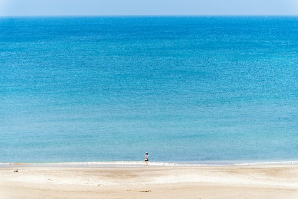 A person stands on the beach, facing the ocean.